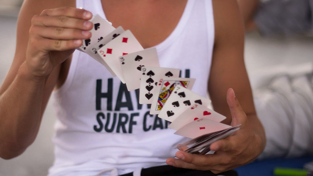 Man in tank top performs card spring card flourish with deck of cards